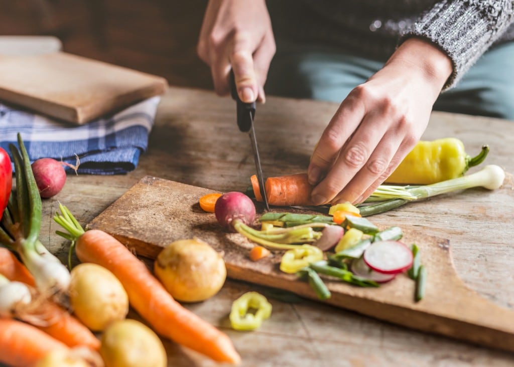 Sur cette photo, on voit une personne occupée à préparer un repas. Elle se tient devant un plan de travail sur lequel sont disposés des aliments et des ustensiles de cuisine. Elle porte un tablier blanc et manie habilement une cuillère en bois pour mélanger les ingrédients. Les odeurs qui s'échappent du récipient font naître dans l'air une atmosphère chaleureuse et apaisante.