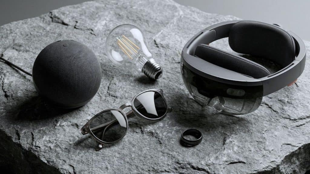Sélection de cinq accessoires technologiques modernes incluant une enceinte, une bague connectée et un casque de réalité mixte sur une surface sobre.