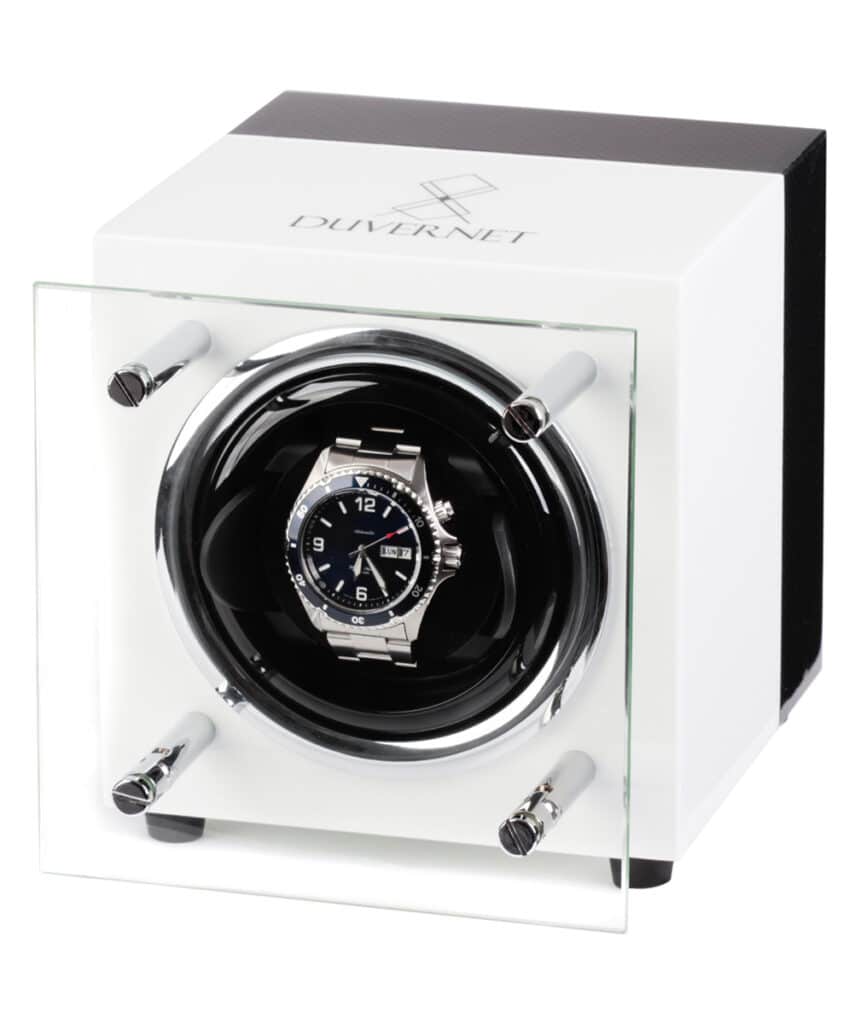 Sur cette image, on voit un objet d'aspect mécanique qui ressemble à une boîte carrée dotée de boutons et de leviers. Il est constitué de métal et recouvert d'un revêtement noir luisant avec des touches chromées. On peut voir un grand volant argenté sur le côté droit, ce qui semble indiquer qu'il sert à régler la tension d'une montre.