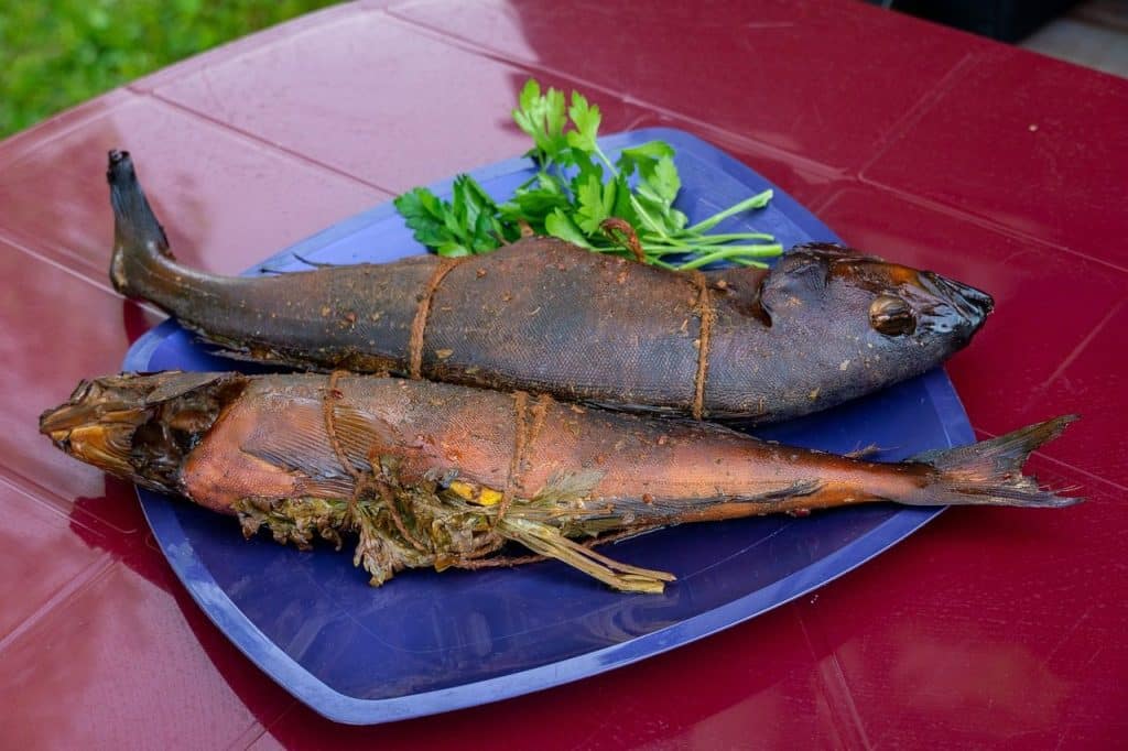Deux poissons entiers fumés à chaud présentés sur une assiette bleue avec des brins de persil frais.